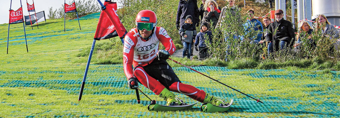 A man skis on grass instead of snow.
