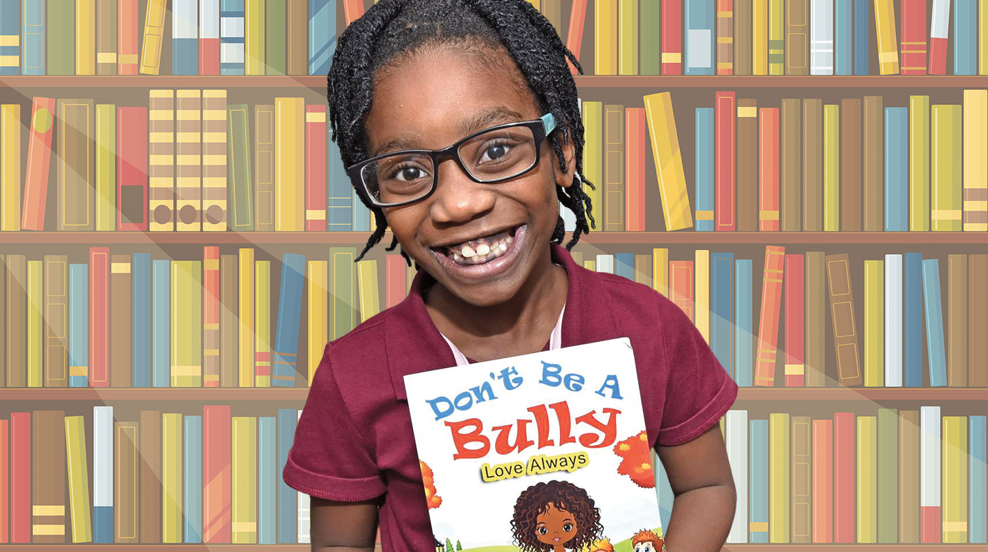 A young kid smiles while holding a book titled Don’t be a bully.